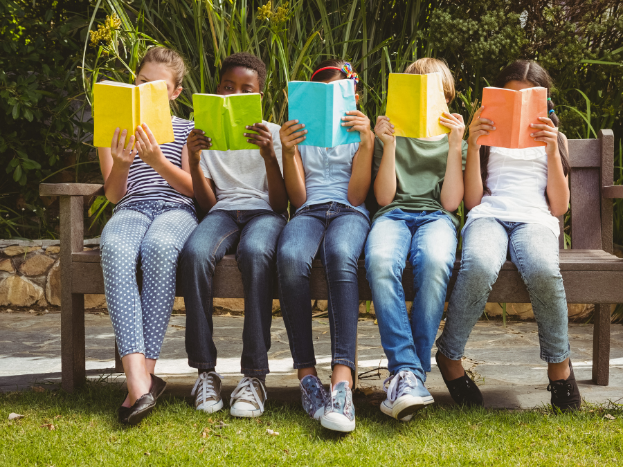 Five kids sit on a park bench reading