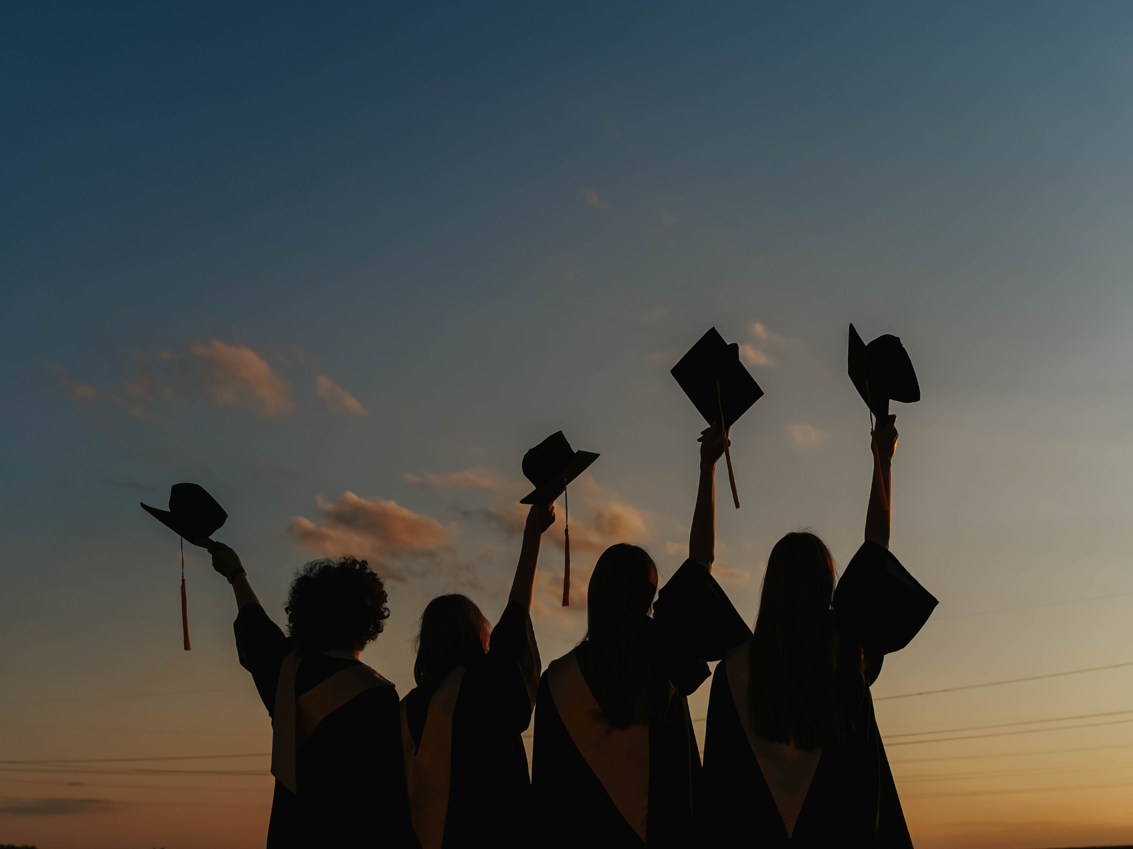 Graduates with their caps held over their heads. 